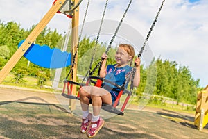 Happy child girl on swing on warm and sunny day outdoors. Little kid playing on nature walk in playground in park, cute blond girl