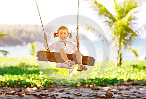 Happy child girl swinging on swing at beach in summer