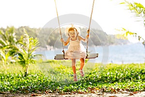 Happy child girl swinging on swing at beach in summer