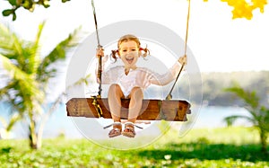 Happy child girl swinging on swing at beach in summer