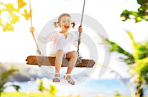 Happy child girl swinging on swing at beach in summer