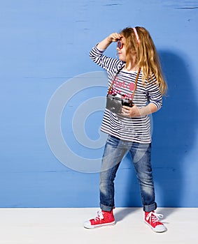 Happy child girl tourist with retro camera at the blue wall