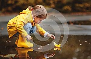 Happy child girl with umbrella and paper boat in puddle in a