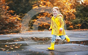 Happy child girl with an umbrella and rubber boots in puddle on