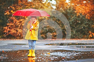 Happy child girl with an umbrella and rubber boots in puddle on