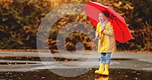Happy child girl with an umbrella and rubber boots in puddle o