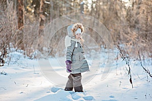 Happy child girl on the walk in winter forest standing and looking out of camera