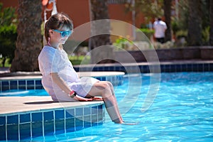 Happy child girl in white dress relaxing on swimming pool side on sunny summer day