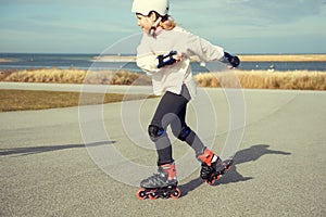 Happy child girl in white helmet, inline skates and safety equipment having fun during skating at sunny day