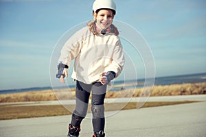 Happy child girl in white helmet, inline skates and safety equipment having fun during skating at sunny day