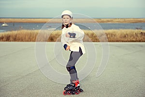 Happy child girl in white helmet, inline skates and safety equipment having fun during skating at sunny day