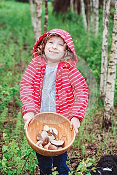 Happy child girl with wild edible wild mushrooms on wooden plate