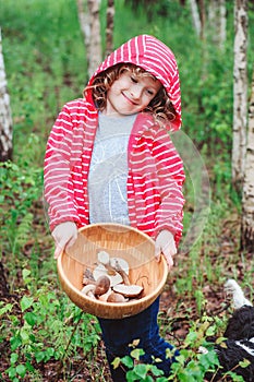 Happy child girl with wild edible wild mushrooms on wooden plate