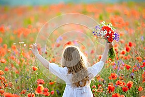 Happy child girl with wild field flowers running thru meadow in