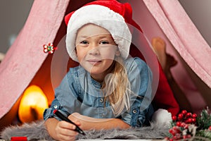 Happy child girl writes a list of gifts and wishes. Letter to Santa Claus on Christmas and New Years Eve