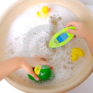 happy child, girl 3 years old plays with rubber green, yellow ducks for swimming, plastic boat, child's toys in soapy foam,
