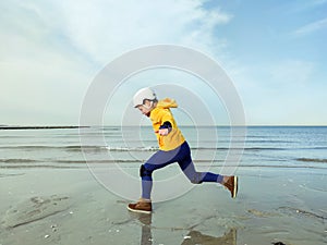 Happy child girl in yellow pullover in helmet and inline protective equipment running and having fun on beach on Baltic sea