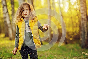 Happy child girl in yellow vest walking in summer sunny forest