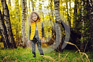 Happy child girl in yellow vest walking in summer sunny forest