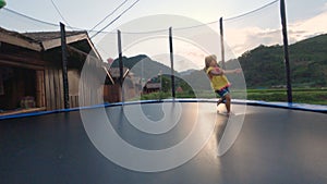Happy child girls playing and jumping on trampoline outdoor at sunset.