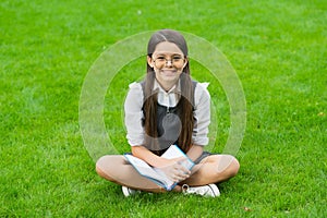 happy child in glasses reading book sitting on green grass