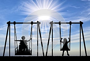 Happy child is handicapped in a wheelchair on an adaptive swing having fun with a healthy child together