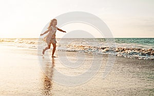 Happy child having fun running on the beach at sunset - Adorable little girl playing along the sea water