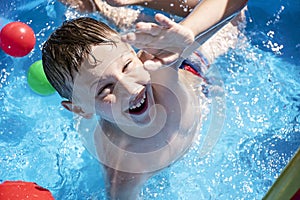 Happy child having fun in the summer time. Boy jumping into the swimming pool and looking into the camera. Holiday. Kid on