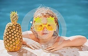 Happy child having fun at swimming pool on sunny day. Kids summer holidays and vacation concept. Summer pineapple fruit.