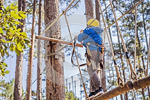 Happy child in a helmet, healthy teenager school boy enjoying activity in a climbing adventure park on a summer day