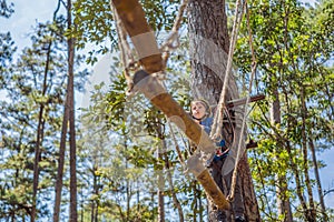 Happy child in a helmet, healthy teenager school boy enjoying activity in a climbing adventure park on a summer day