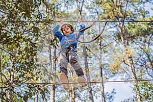 Happy child in a helmet, healthy teenager school boy enjoying activity in a climbing adventure park on a summer day