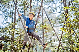 Happy child in a helmet, healthy teenager school boy enjoying activity in a climbing adventure park on a summer day