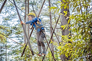 Happy child in a helmet, healthy teenager school boy enjoying activity in a climbing adventure park on a summer day