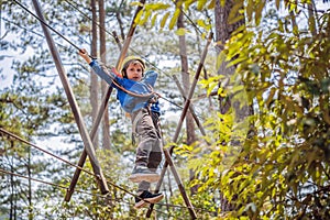 Happy child in a helmet, healthy teenager school boy enjoying activity in a climbing adventure park on a summer day