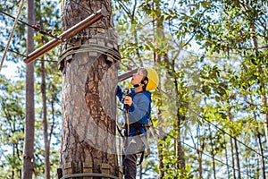 Happy child in a helmet, healthy teenager school boy enjoying activity in a climbing adventure park on a summer day