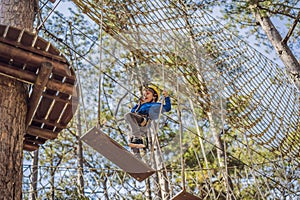 Happy child in a helmet, healthy teenager school boy enjoying activity in a climbing adventure park on a summer day