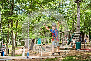 Happy child in a helmet, healthy teenager school boy enjoying activity in a climbing adventure park on a summer day