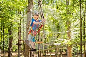 Happy child in a helmet, healthy teenager school boy enjoying activity in a climbing adventure park on a summer day