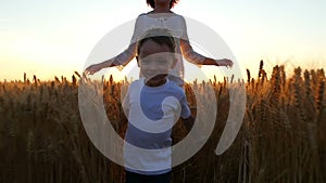 A happy child and his mother are running across a field of wheat during sunset. Camera movement steadicam.