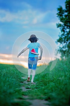 Happy child, holding pair of sneakers in hands, walking on a rural path