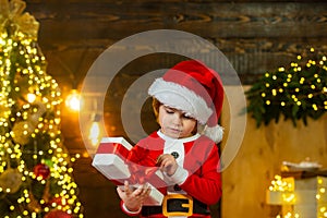 Happy child holding a red gift box with both hands. Portrait of Santa kid with gift looking at camera. Cute little kids