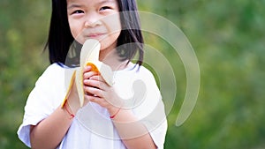 Happy child is holding ripe banana to eat with gusto. Background is natural green. Empty space to enter text