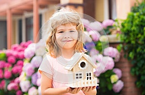 Happy child holding toy house in hands against new home.
