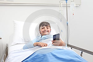 Happy child in hospital bed using smartphone surfs the internet wearing earphones photo
