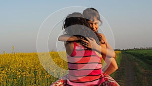 Happy child hugging mother in nature. A woman with a baby hugs in yellow flowers. Mom hugs her daughter. Emotions of the child.