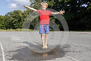 happy child joyfully jumps barefoot into transparent puddle on asphalt on summer day after the rain