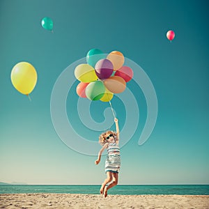 Happy child jumping with colorful balloons on sandy beach