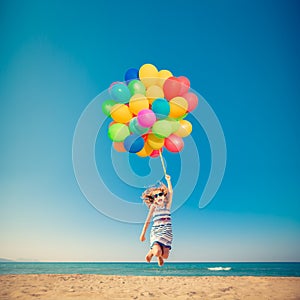 Happy child jumping with colorful balloons on sandy beach