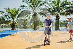 Happy child on kick scooter in on the basketball court. Kids learn to skate roller board. Little boy skating on sunny